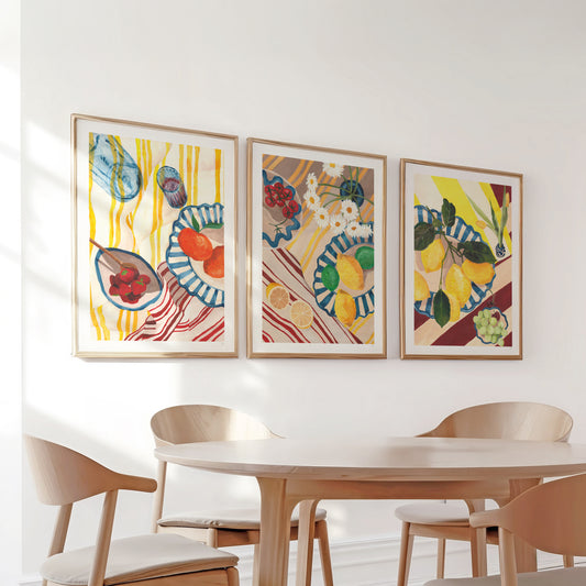 Three colorful framed artworks on a wall above a dining table with chairs.
