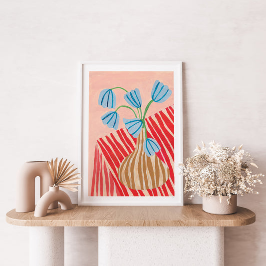 Framed abstract art print with blue flowers and red patterns on a wooden shelf.