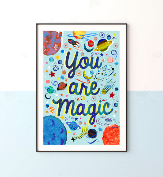 Space illustrated prints with planets and stars with teh words you are magic on a light blue background in a black frame on a blue and white wall
