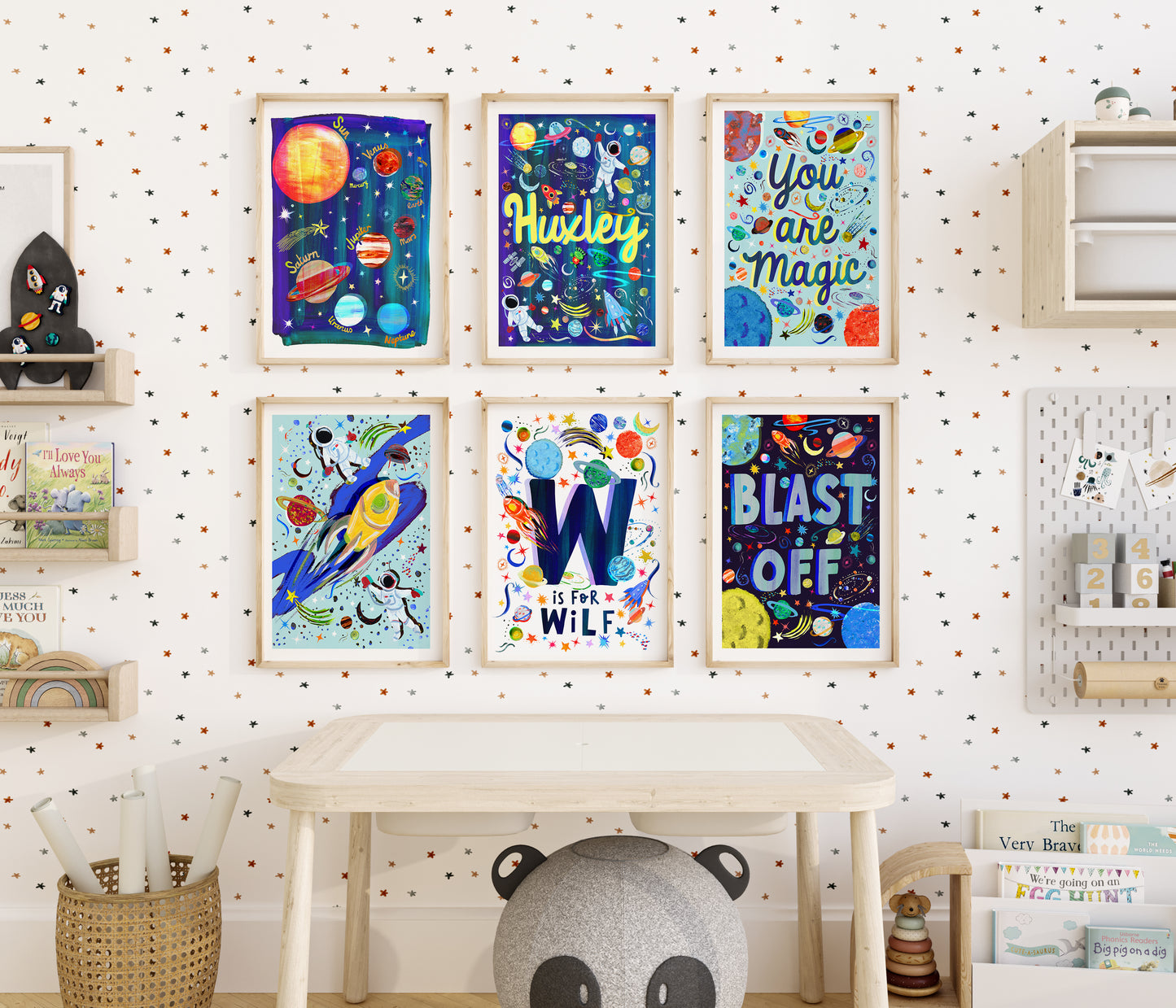 A colourful space themed print set of 6 artworks in a kids bedroom above a desk, displaying 2 different style of personalised space name prints, you are magic, blast off and planets and astronuat prints all hand painted designs on colourful blues, reds, oranges and whites