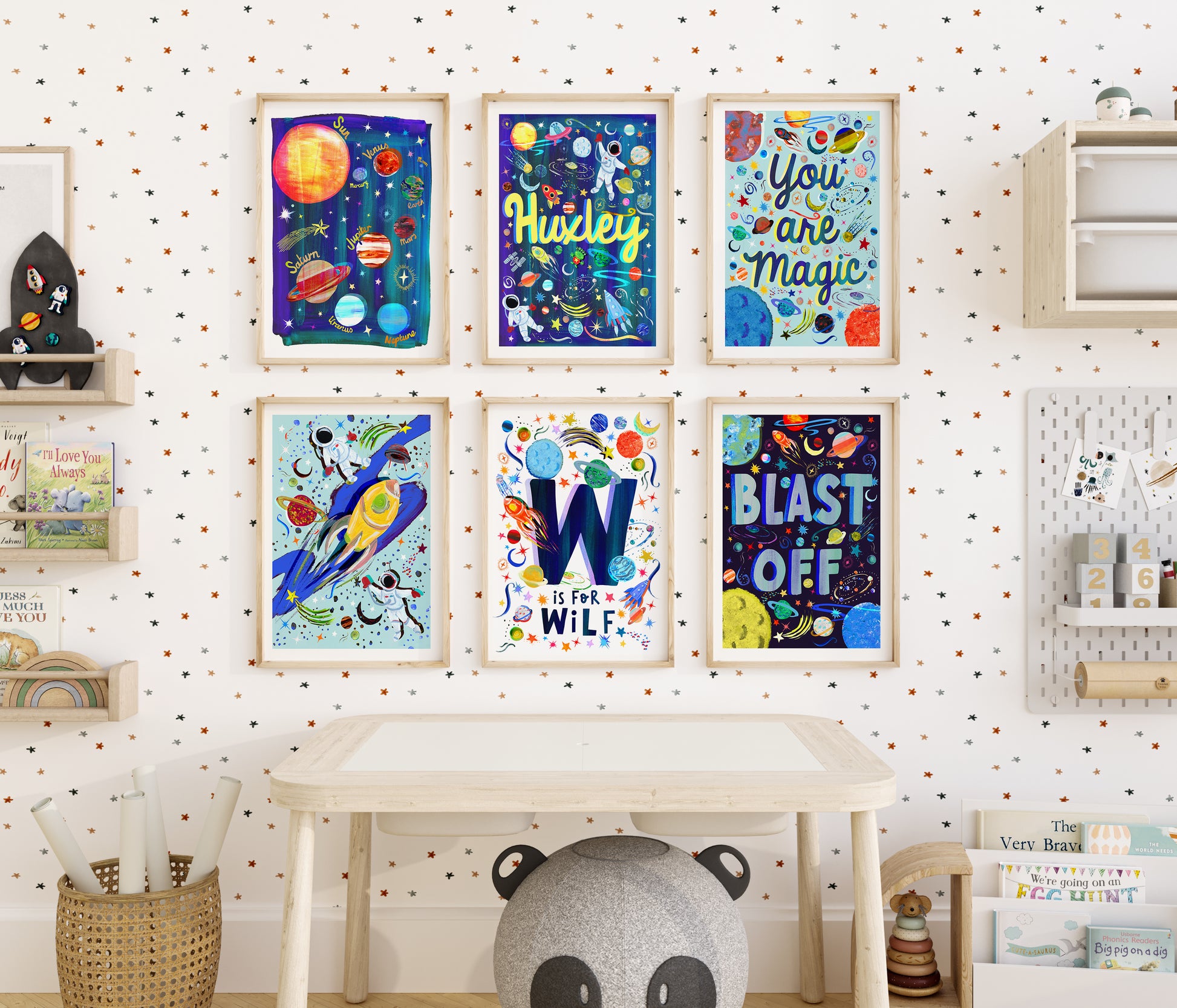 A colourful space themed print set of 6 artworks in a kids bedroom above a desk, displaying 2 different style of personalised space name prints, you are magic, blast off and planets and astronuat prints all hand painted designs on colourful blues, reds, oranges and whites