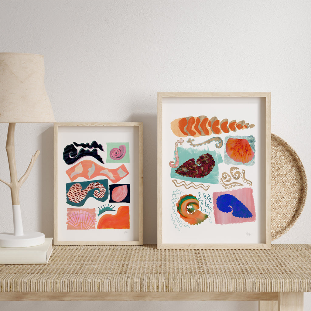 Framed abstract artworks on a table with a lamp and decorative items.