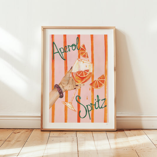 Framed artwork with a glass of Aperol Spritz and orange slices on a striped background.