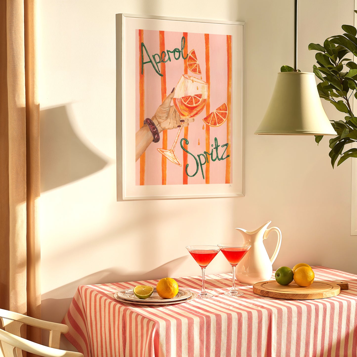 Framed artwork with 'Aperol Spritz' design above a table set with drinks and fruit.