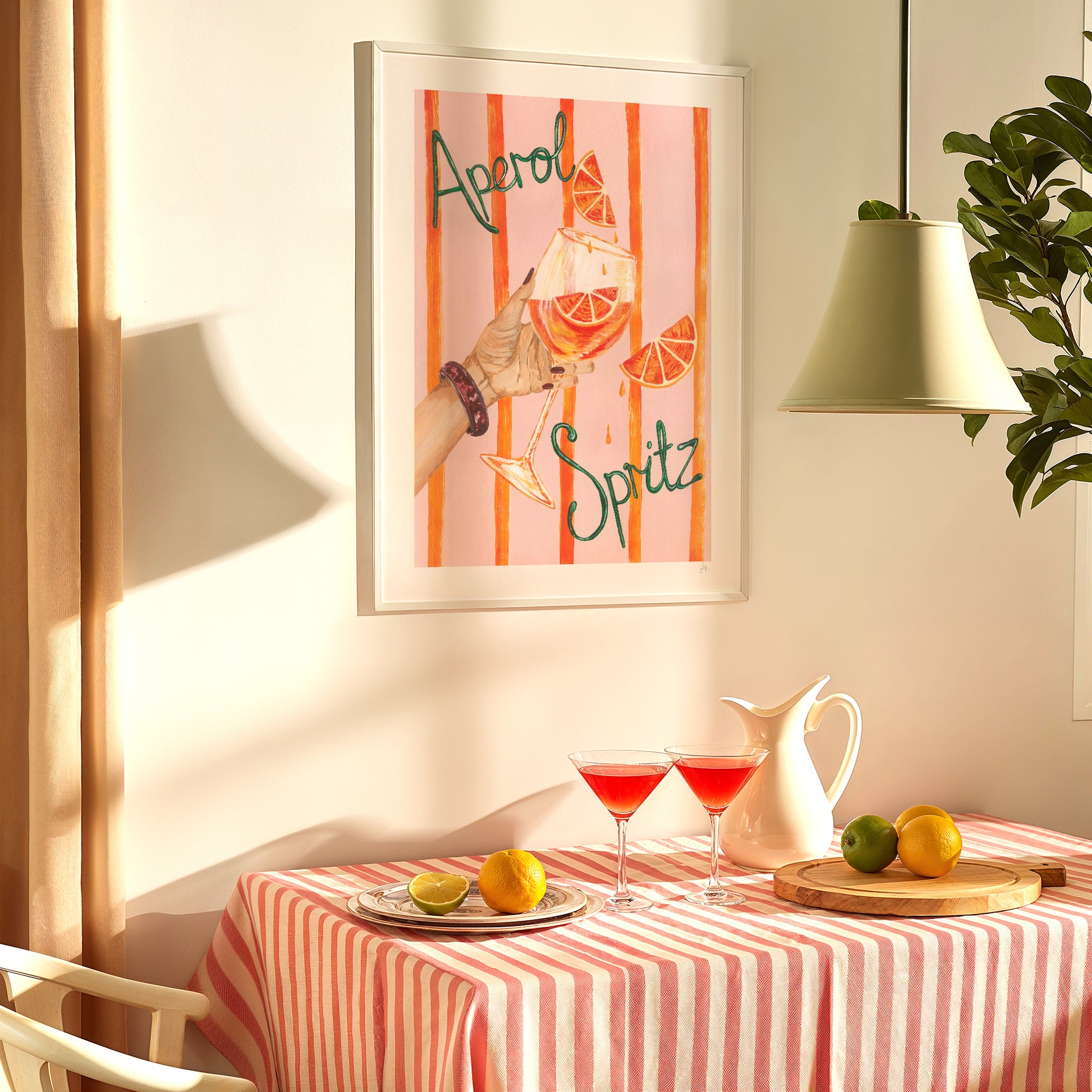 Framed artwork with 'Aperol Spritz' design above a table set with drinks and fruit.