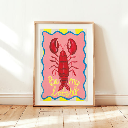 Framed artwork of a red lobster with 'Be my lobster' text on a pink background, leaning against a white wall.