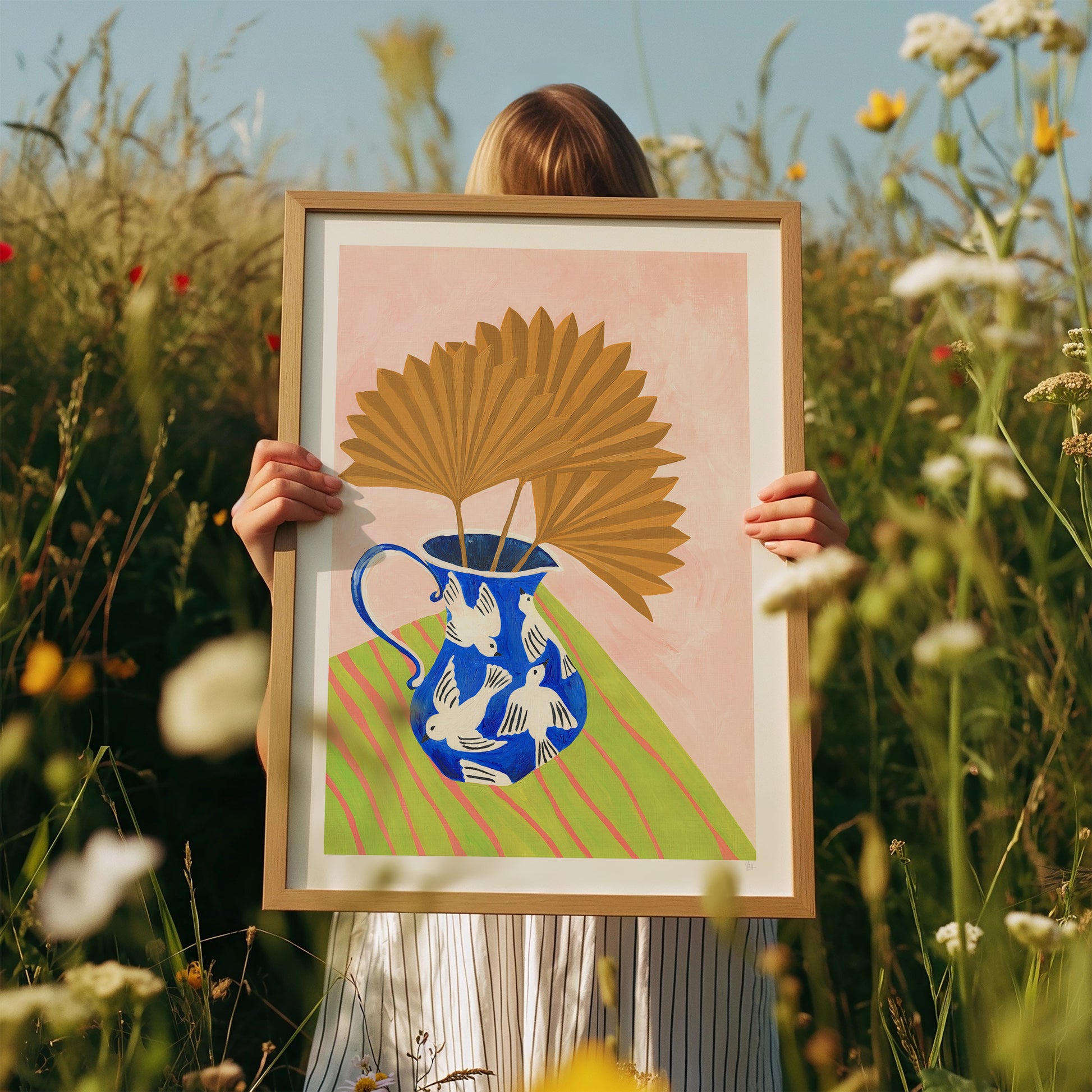 Person holding a framed artwork with a floral design in a field of flowers