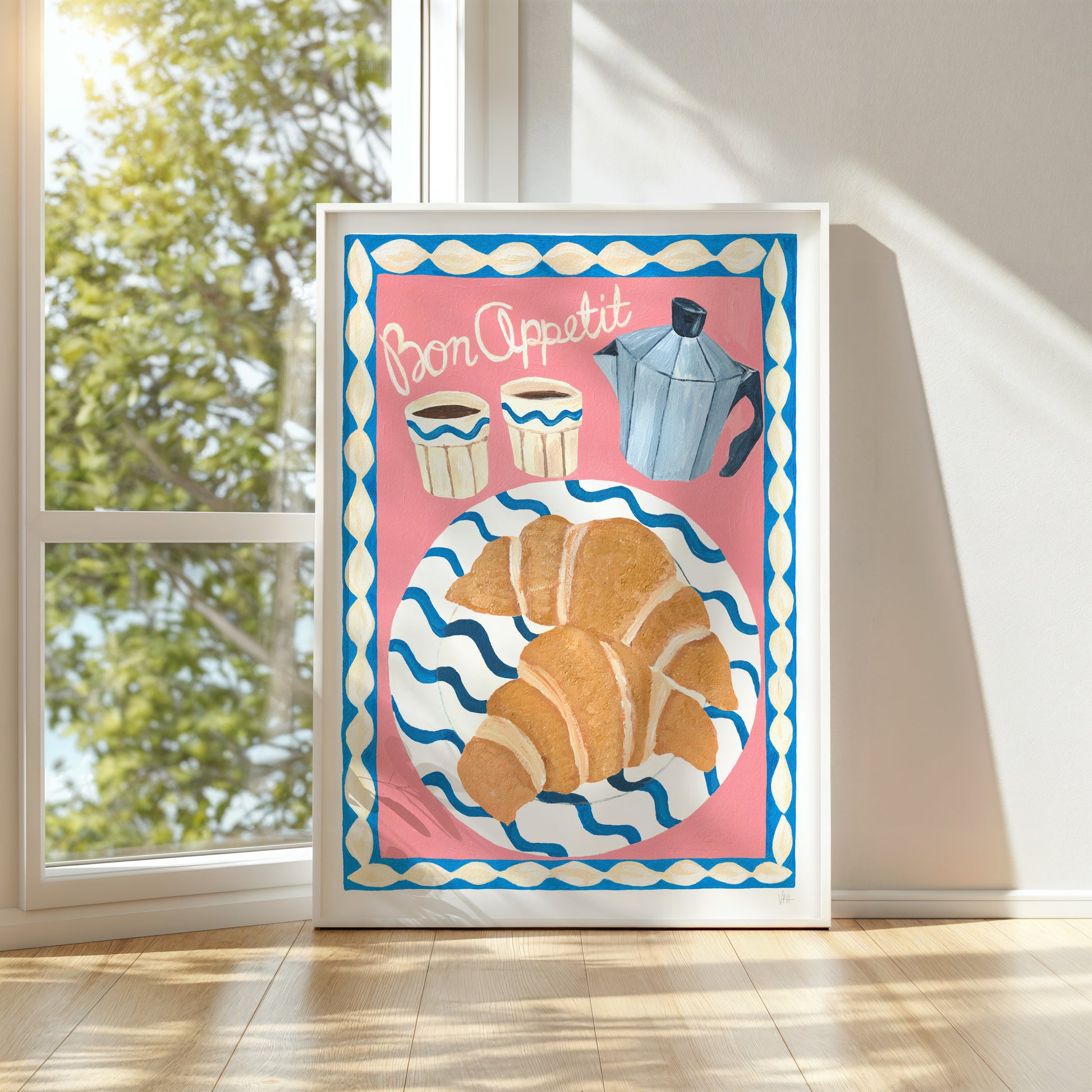 Decorative kitchen print with croissants and coffee pots on a pink background, framed and leaning against a wall.
