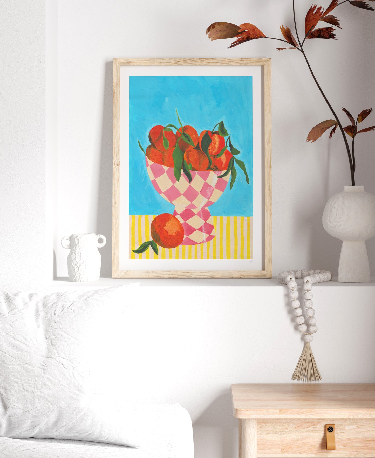 Framed artwork of oranges in a checkered bowl on a wall above a white sofa.