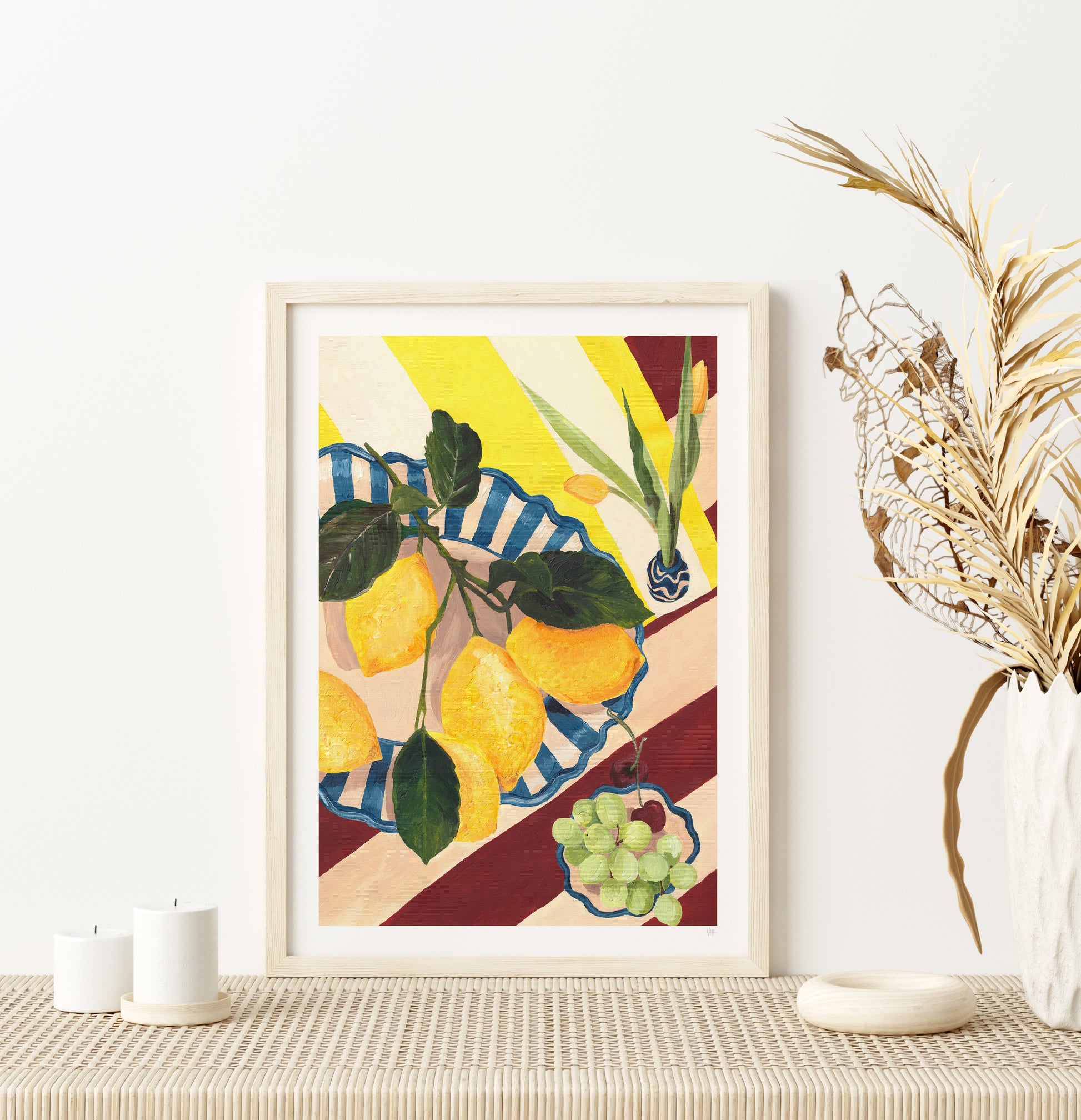 Framed artwork of lemons and grapes on a table with decorative elements.