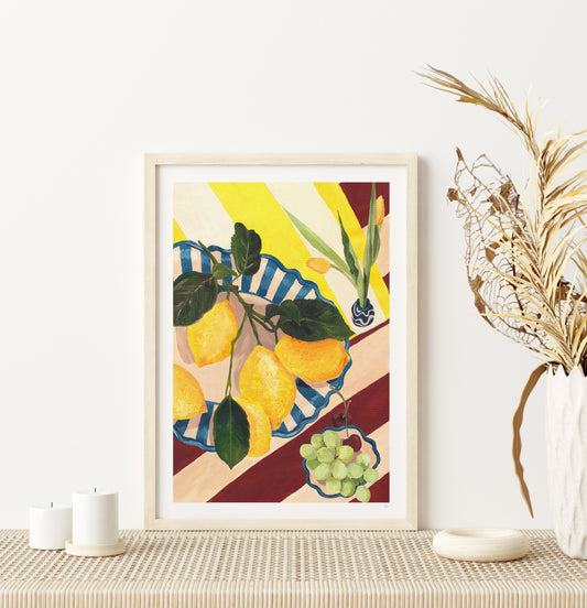 Framed artwork of lemons and grapes on a table with decorative elements.