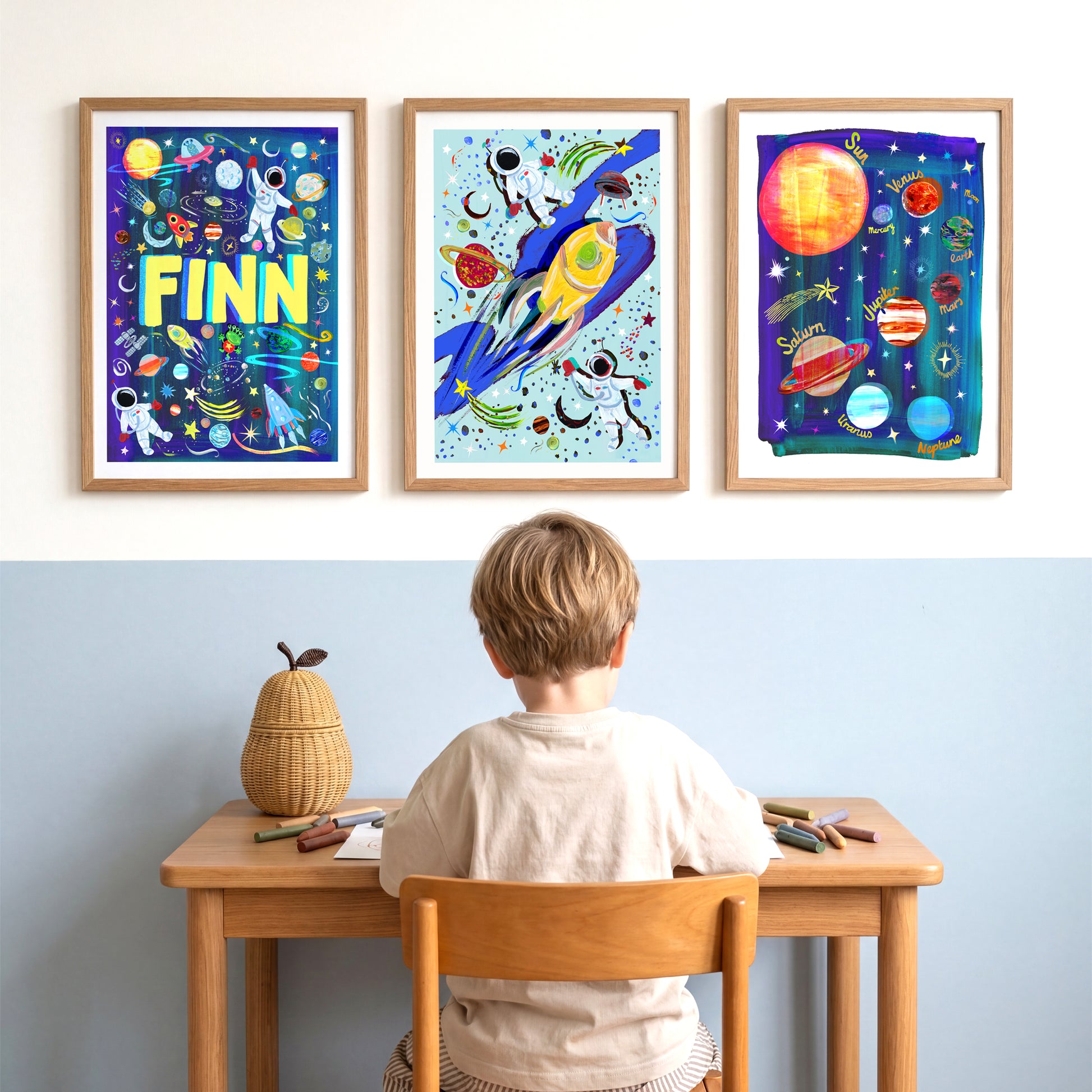 Three framed space-themed artworks on a wall above a child at a desk.