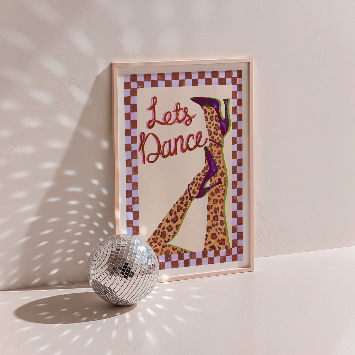 Framed artwork with 'Let's Dance' text and a leopard print shoe design, next to a disco ball on a light background.