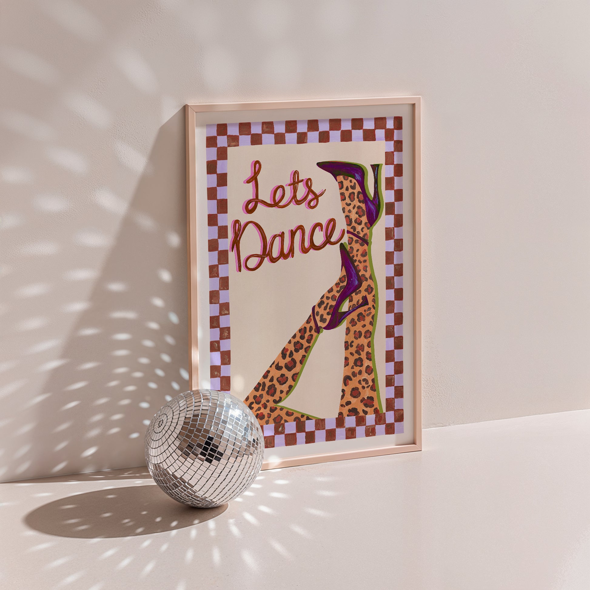 Framed artwork with 'Let's Dance' text and a leopard print shoe design, next to a disco ball on a light background.