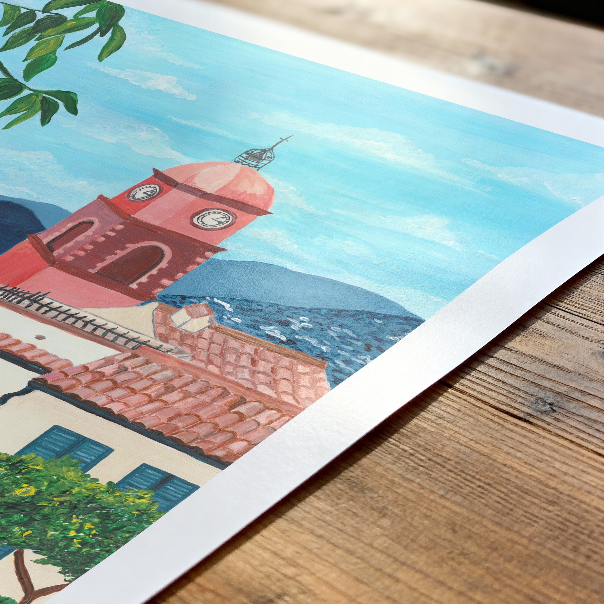 Colorful illustration of a coastal scene with buildings and a clock tower on a wooden surface.