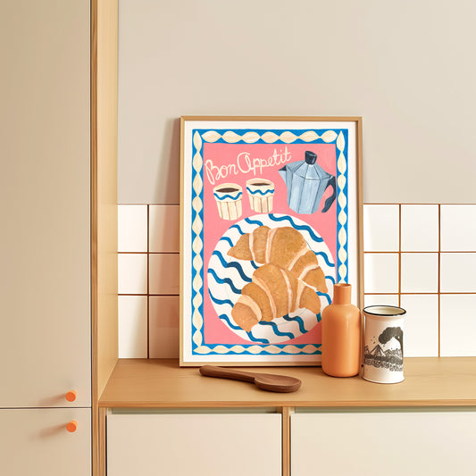 Framed artwork with a croissant and coffee pot design on a kitchen counter.