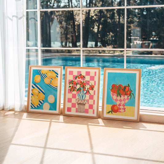 Three colorful framed artworks on a windowsill with a pool view outside.