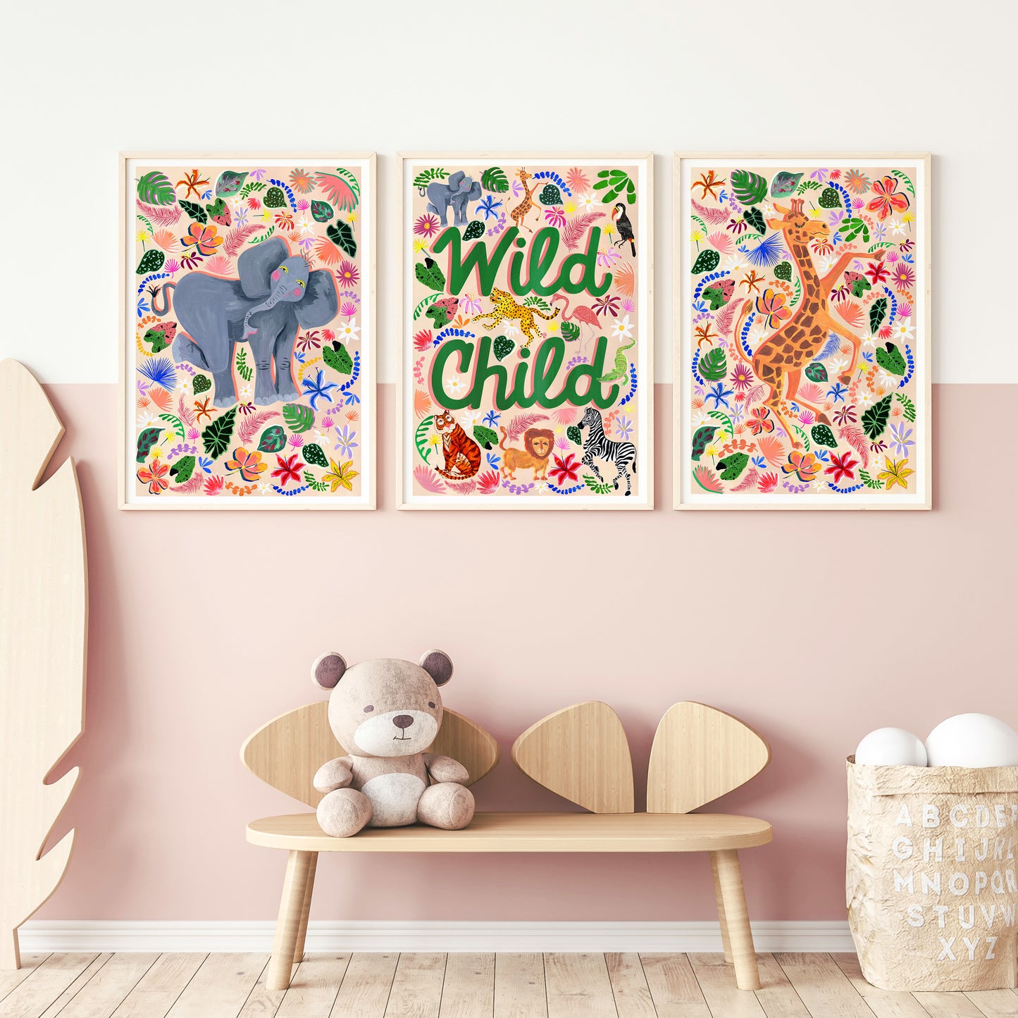 Three colorful animal-themed wall art prints on a pink wall with a wooden bench and teddy bear.