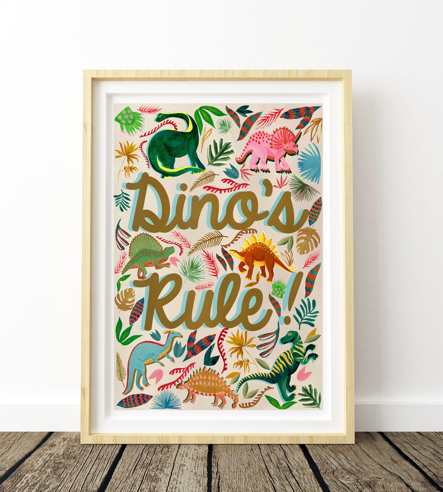 Framed poster with colorful dinosaur illustrations and 'Dinos Rule!' text on a wooden floor.