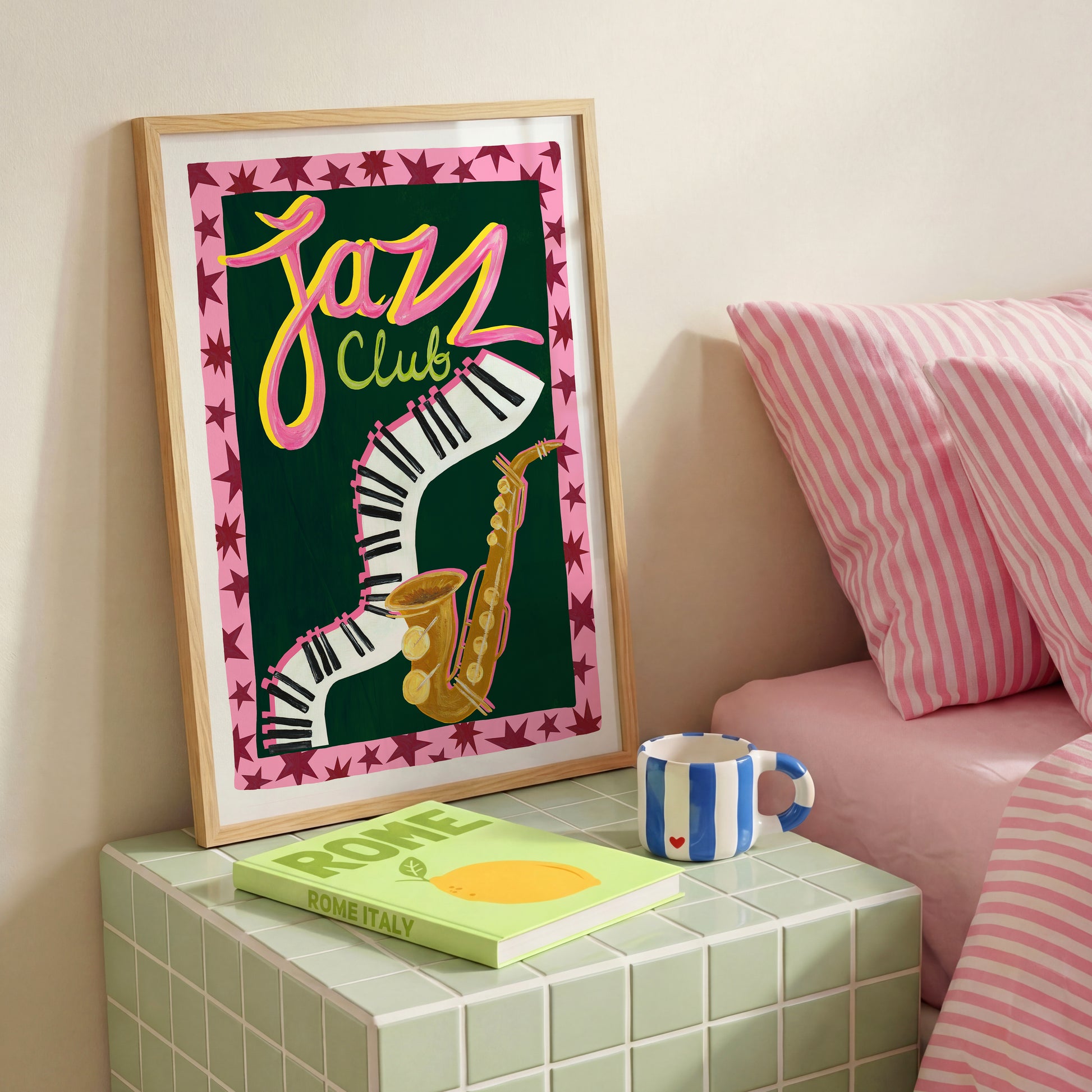 Framed 'Jazz Club' poster on a nightstand with a book and mug.