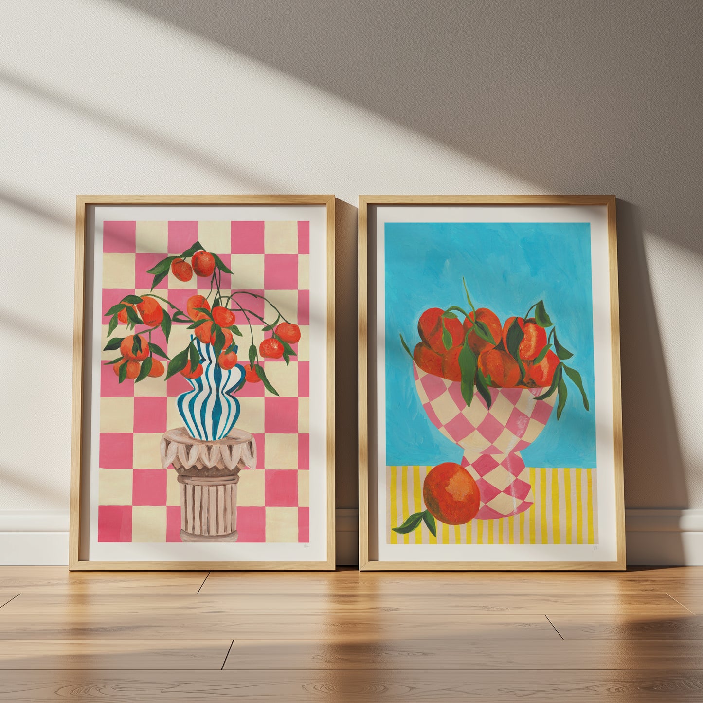 Two framed artworks on a wooden floor with a neutral wall background