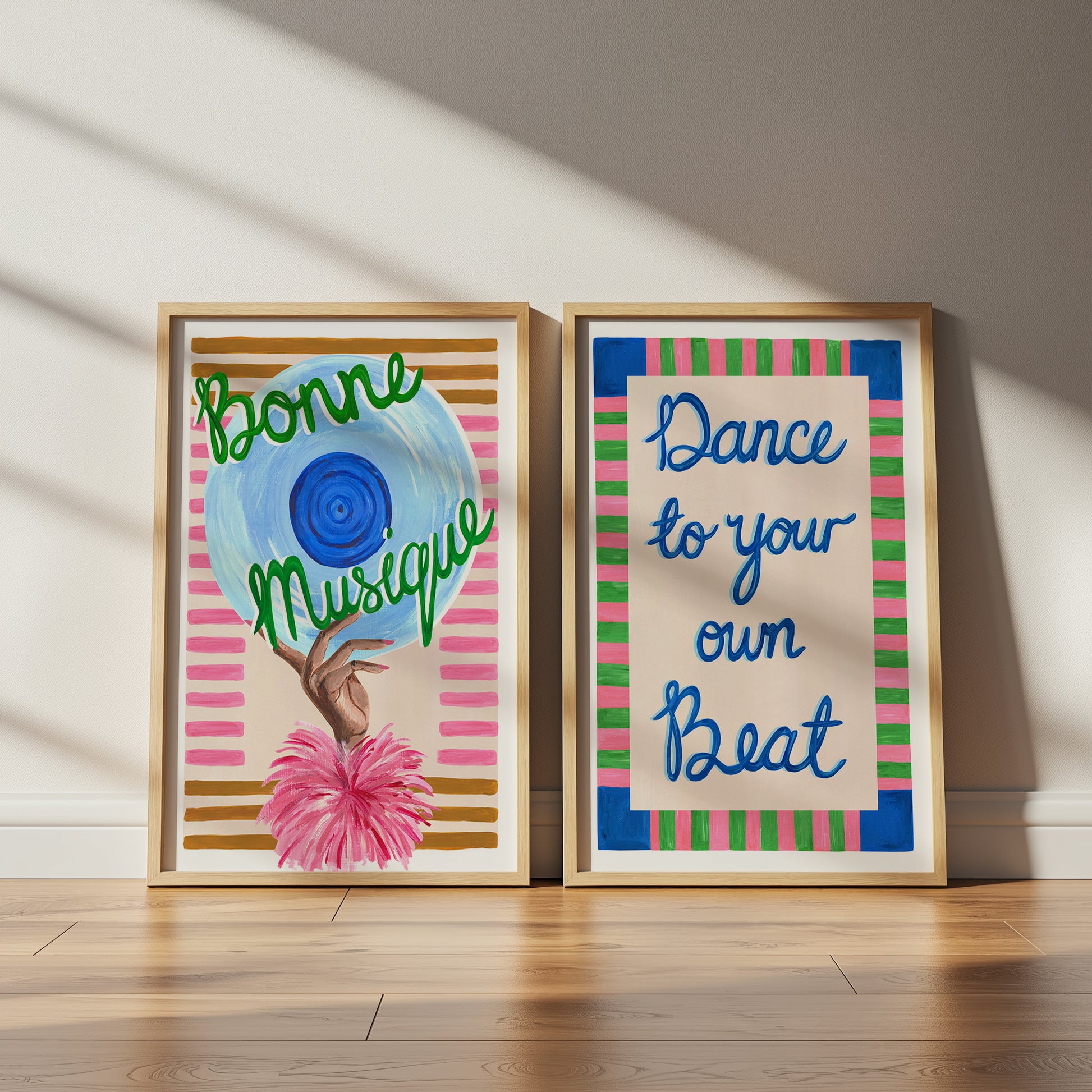 Two framed art prints on a wooden floor with a neutral wall background