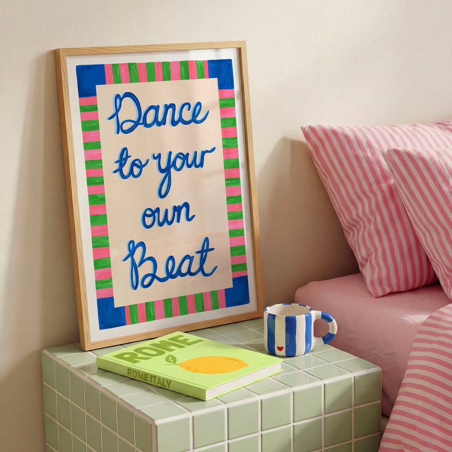 Framed artwork with 'Dance to your own beat' text on a nightstand next to a book and mug.