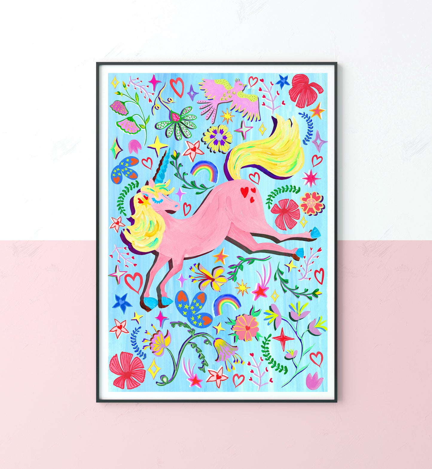 A colourful unicorn illustrations with flower , star and rainbow elements in a black frame place on a white and pink wall