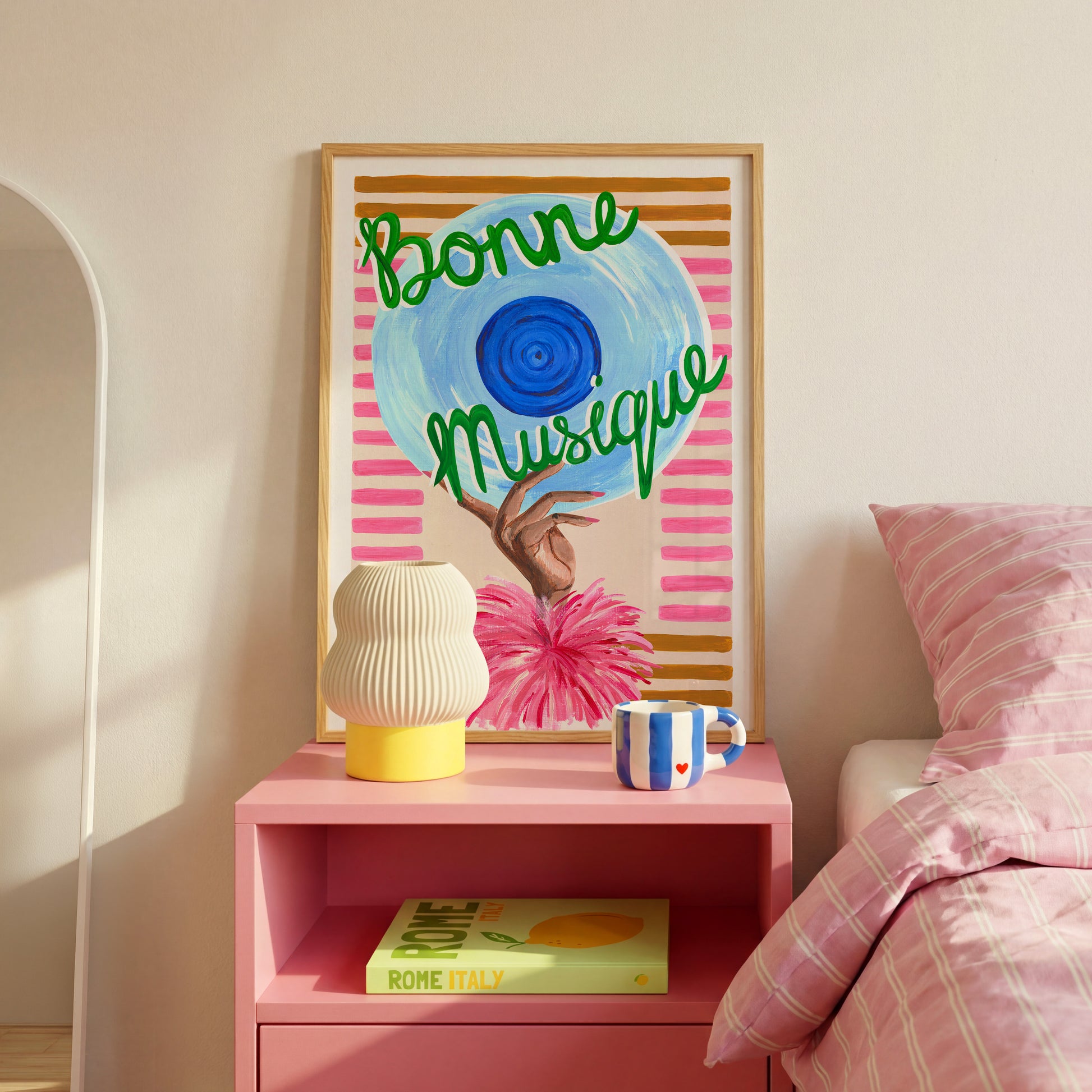 Pink nightstand with decorative items and a colorful framed artwork on a wall.
