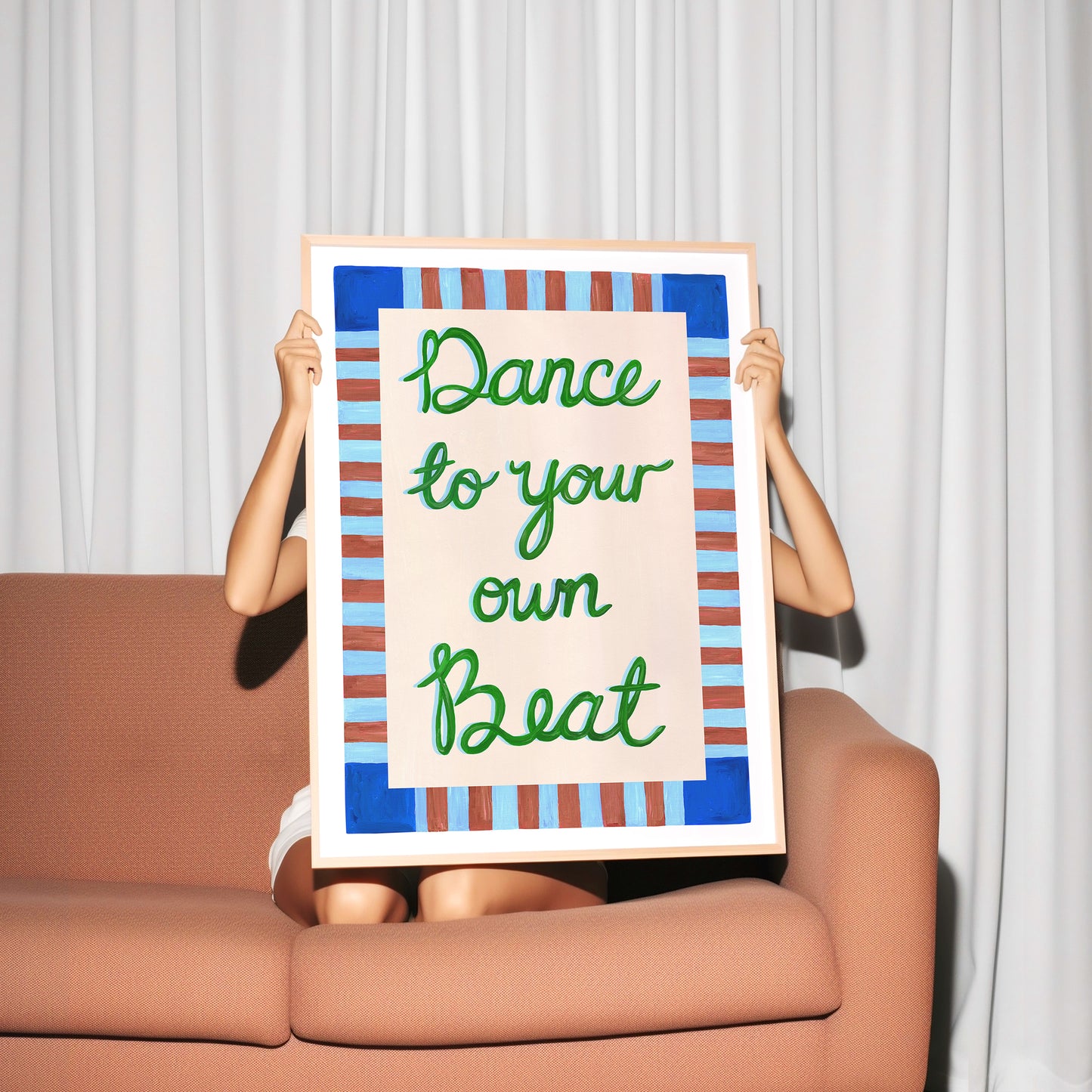 Person holding a framed poster with 'Dance to your own beat' text against a white curtain background.