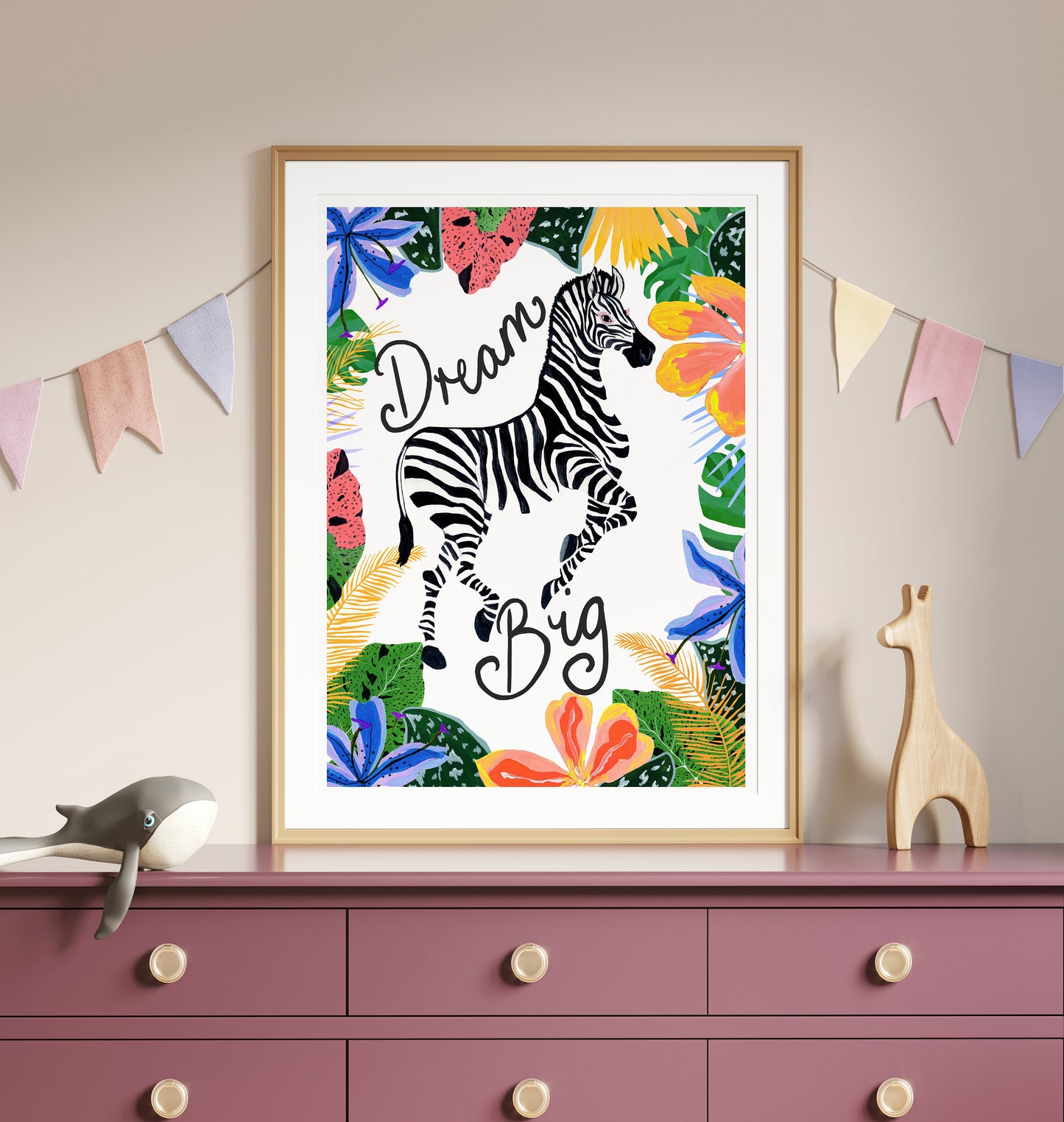 Framed artwork with a zebra and 'Dream Big' text on a colorful leafy background, displayed on a dresser.