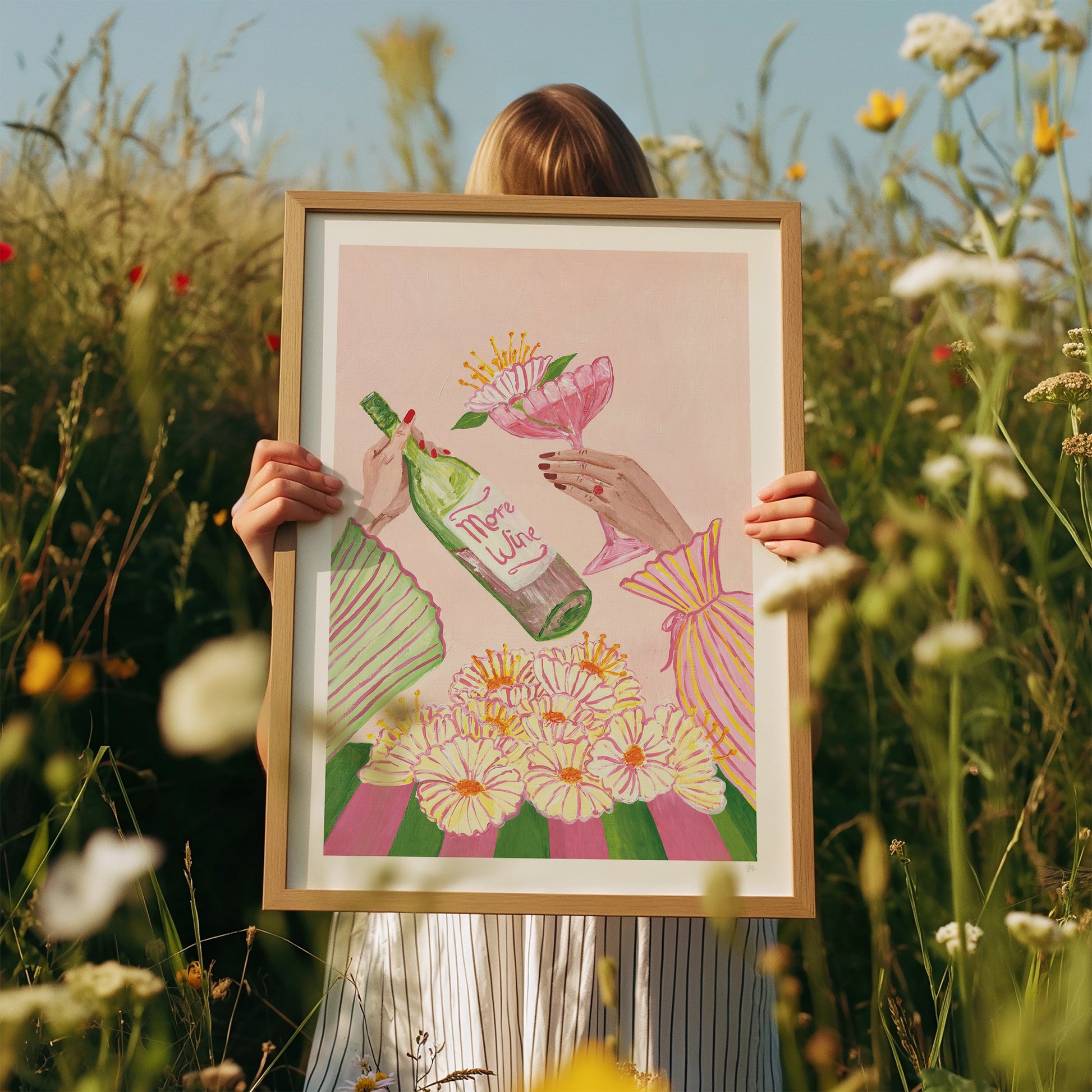 Person holding a framed illustration in a field of flowers