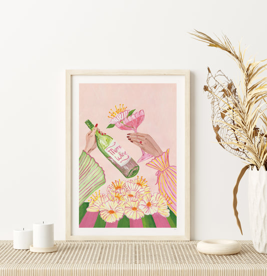 Framed artwork of hands holding a bottle and a pink cocktail with flowers on a pink background, displayed on a table.