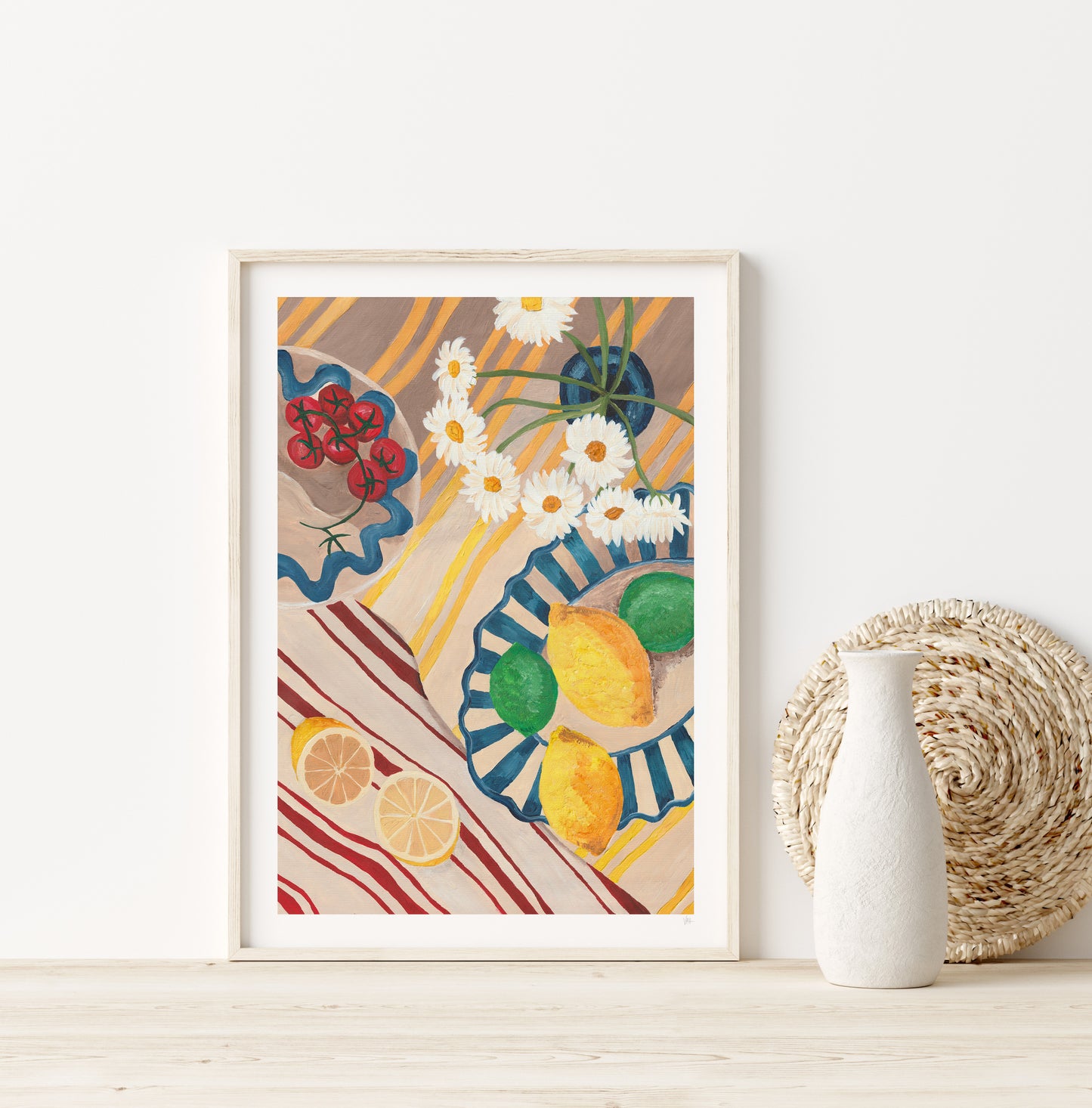 Framed artwork with colorful design of lemons, flowers, and plates on a white wall.