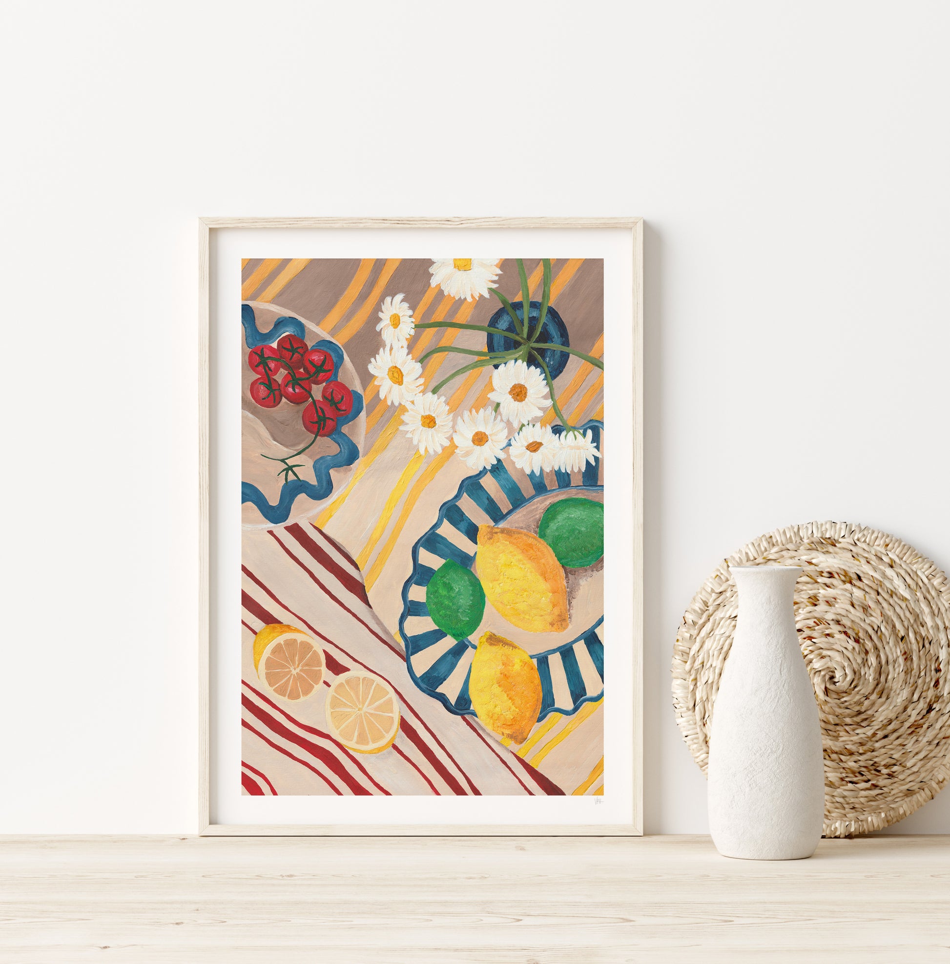 Framed artwork with colorful design of lemons, flowers, and plates on a white wall.