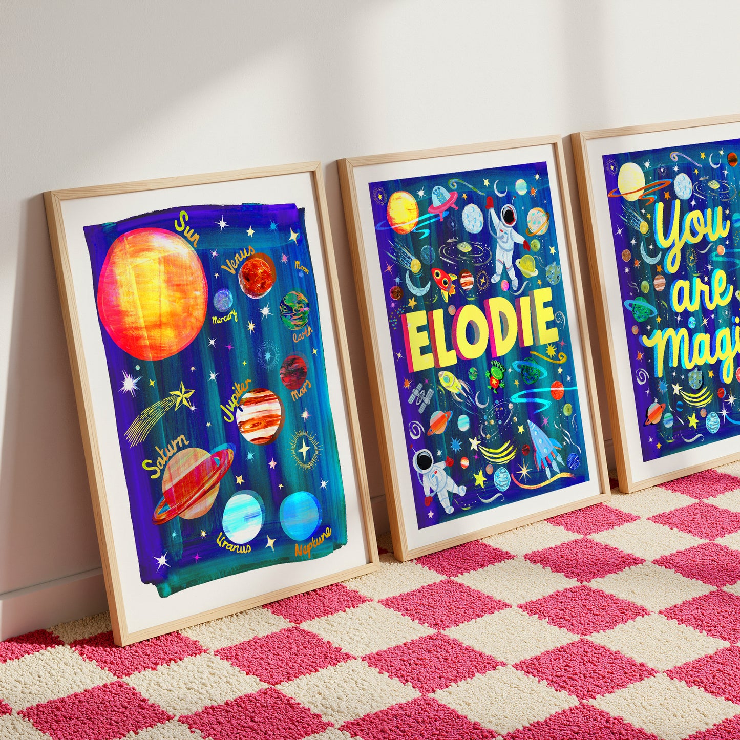 Three framed space-themed artworks on a pink and white checkered rug.