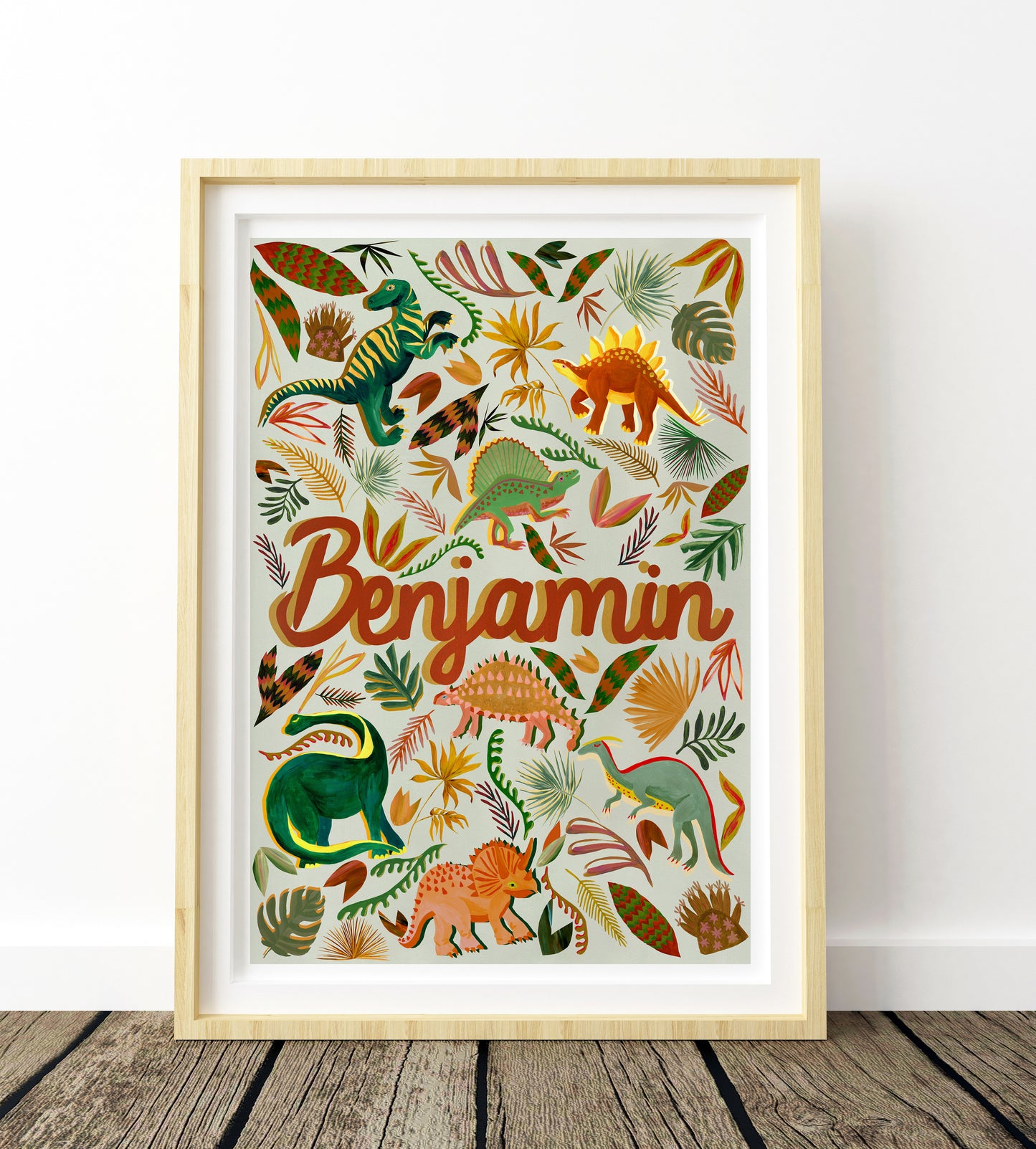 Framed artwork with colorful dinosaur illustrations and the name 'Benjamin' on a white background.
