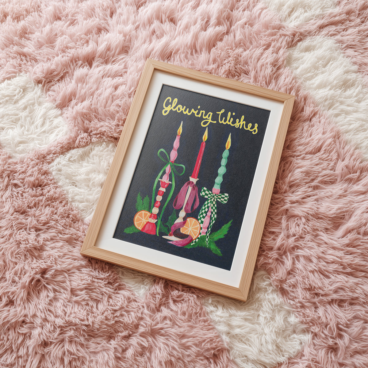 A framed art print featuring three colorful glowing candles on a dark background with the text 'Glowing Wishes' in gold, styled on a fluffy pink and cream rug.