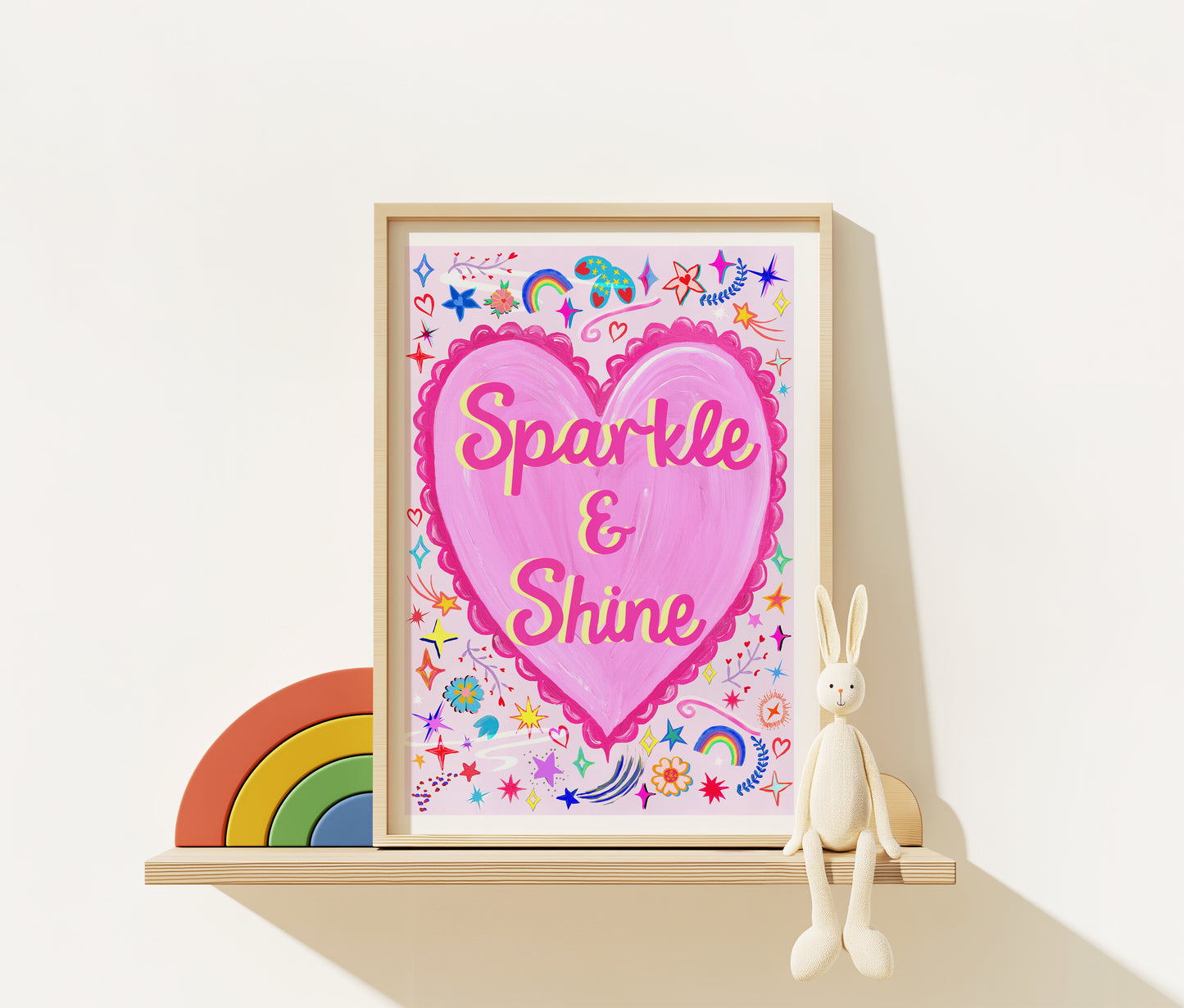 Framed artwork with a pink heart and 'Sparkle & Shine' text, surrounded by decorative elements on a white surface.