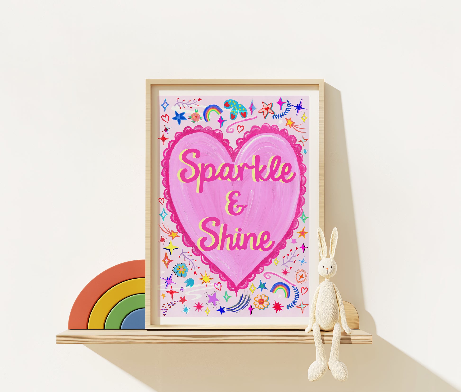 Framed artwork with a pink heart and 'Sparkle & Shine' text, surrounded by decorative elements on a white surface.