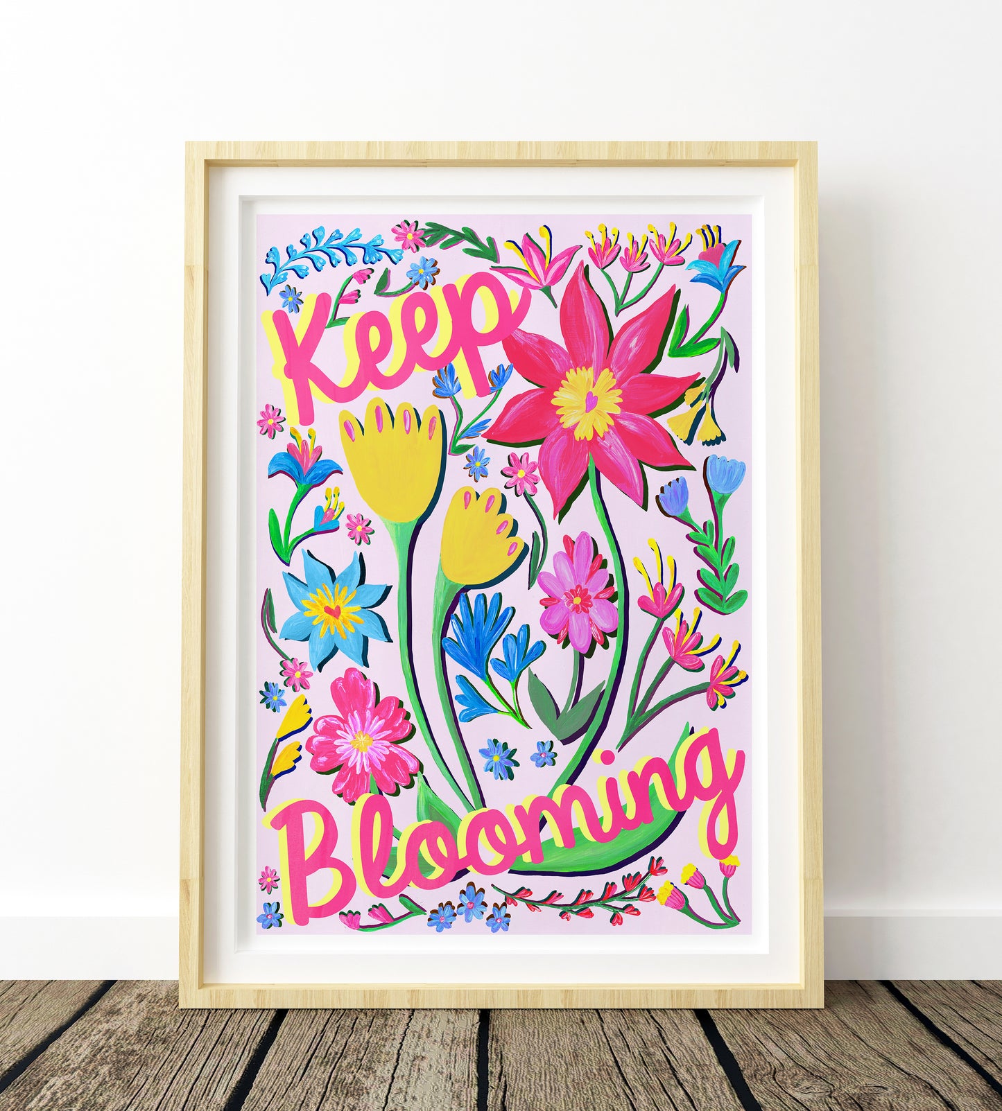 Colorful floral artwork with 'Keep Blooming' text in a wooden frame on a white wall.