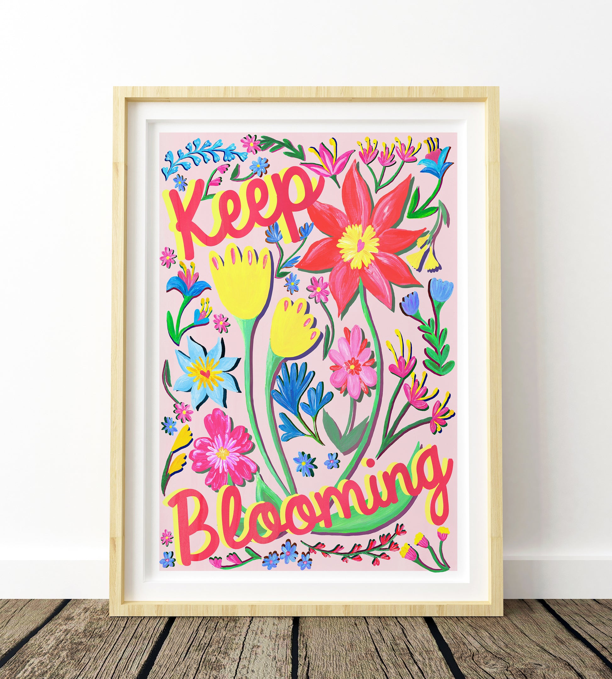 Colorful floral artwork with 'Keep Blooming' text in a wooden frame on a white wall.