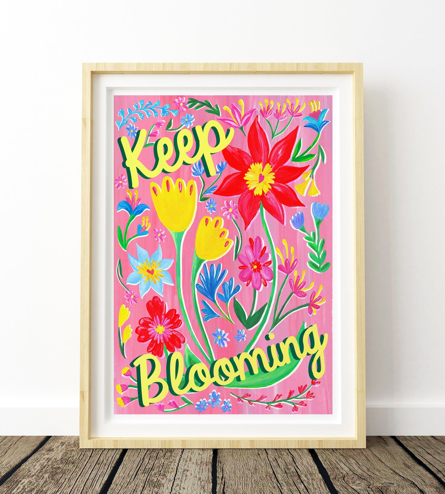 Framed colorful artwork with flowers and 'Keep Blooming' text on a pink background.
