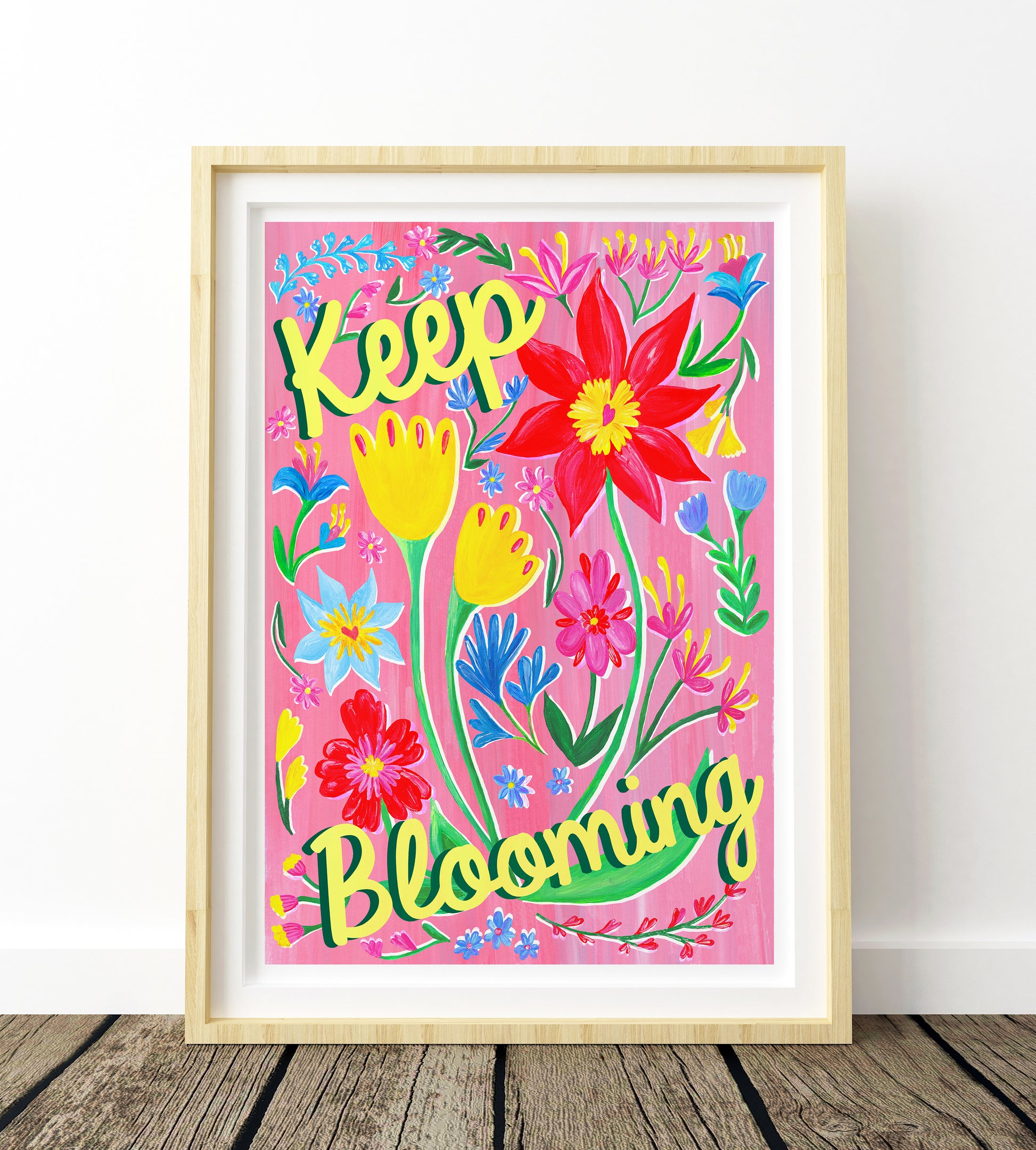 Framed colorful artwork with flowers and 'Keep Blooming' text on a pink background.