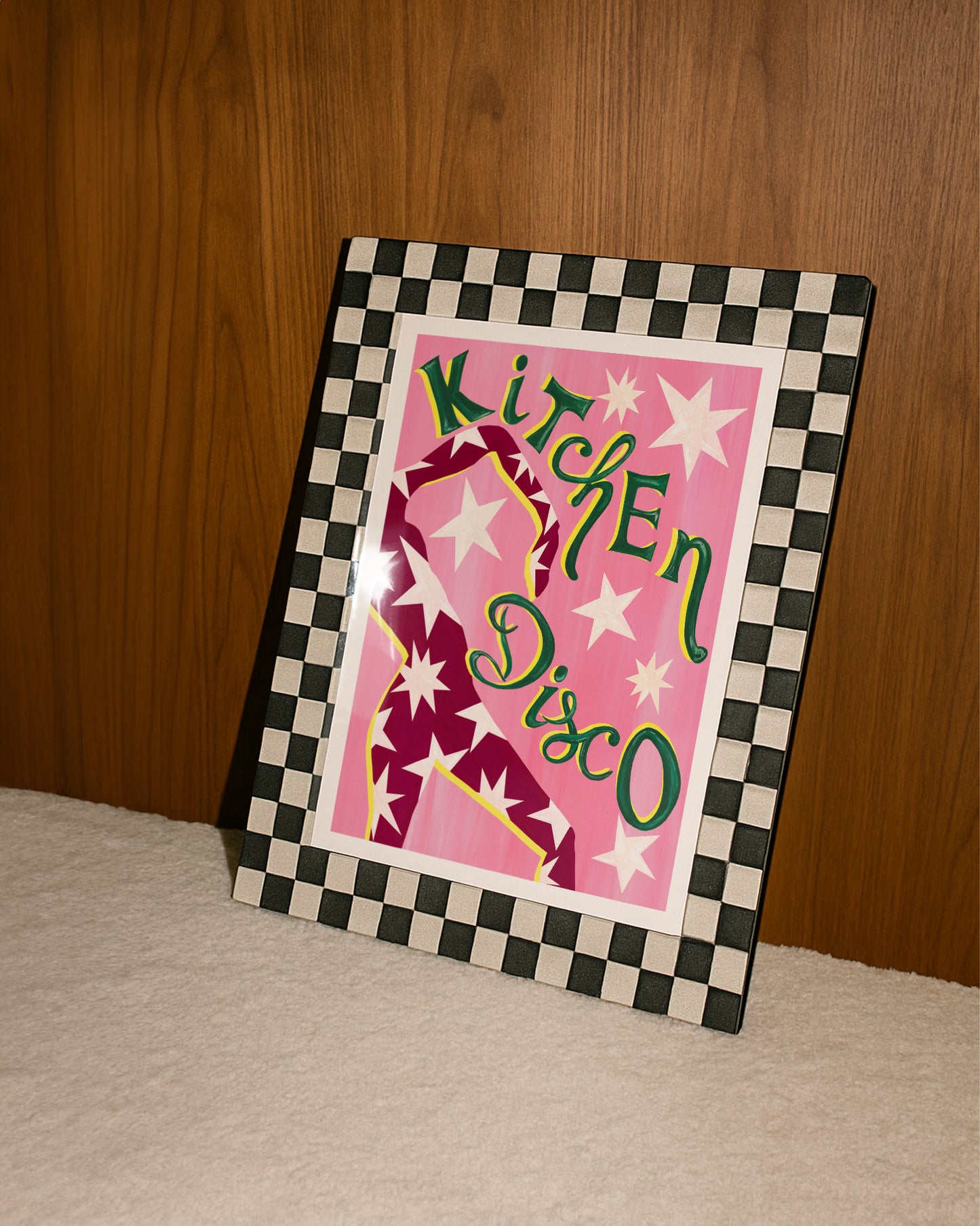 Framed artwork with 'Kitchen Disco' text and checkered border on a wooden surface.