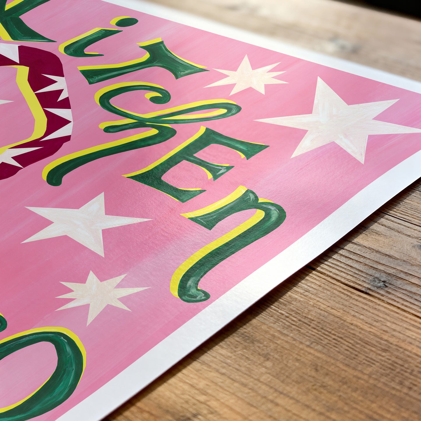 Colorful sign with stars and text on a pink background, placed on a wooden surface.