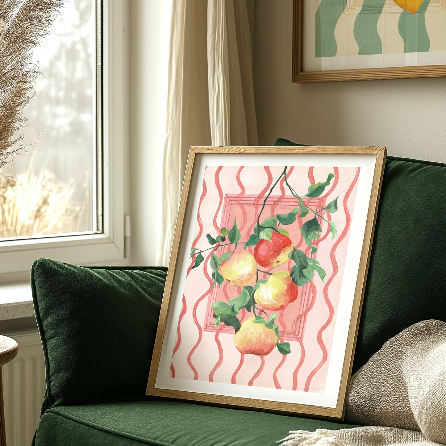 Framed artwork of apples on a pink background on a green couch.