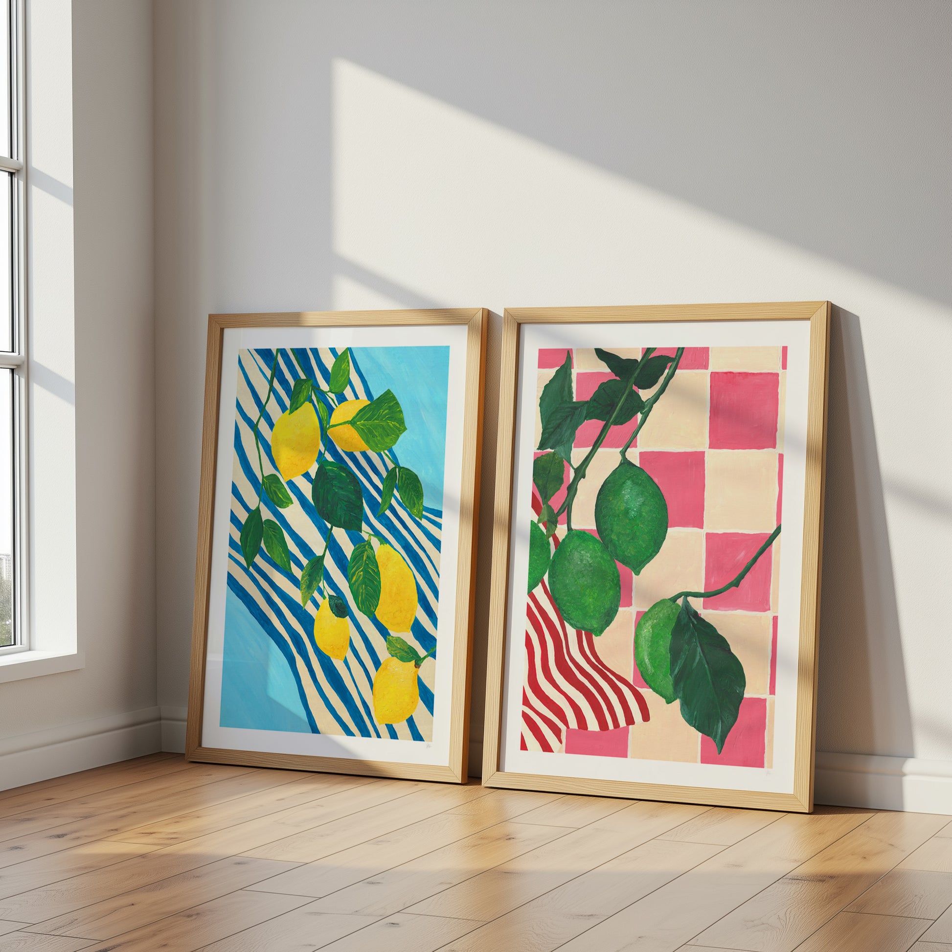 Two framed artworks of lemons and leaves on a wall with sunlight casting shadows.