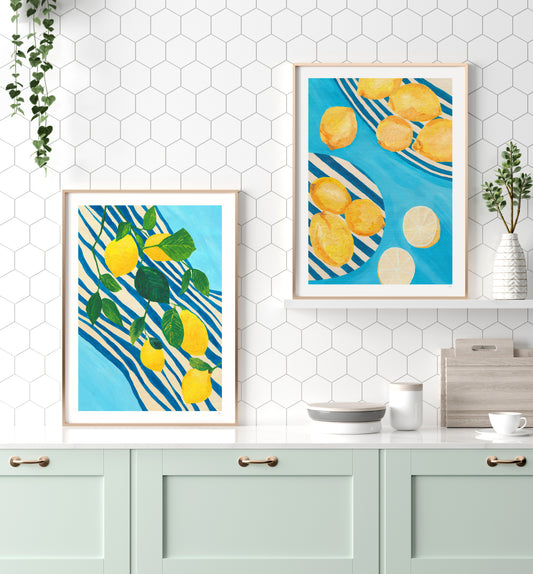 Two framed lemon prints on a kitchen wall with a white countertop and cabinets.