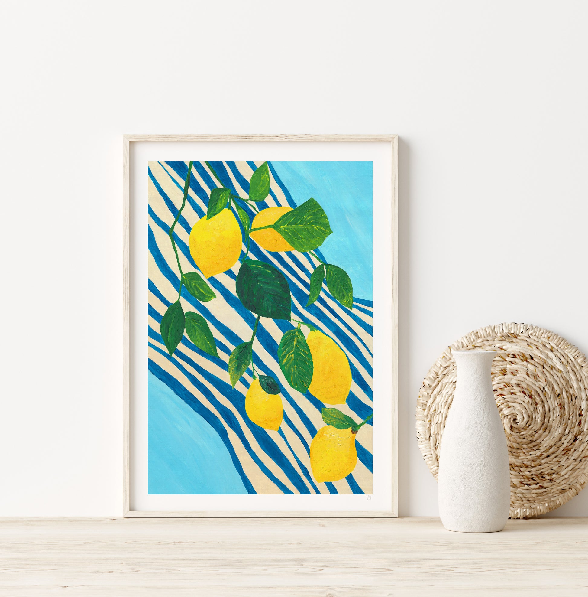 Framed artwork with lemons on a blue and cream stripe towel set against a blue wall.